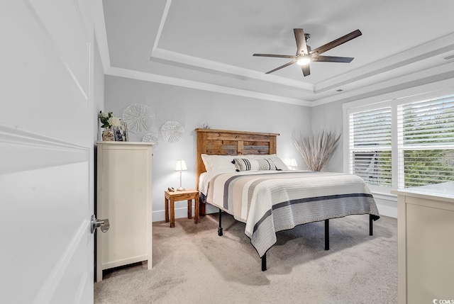 bedroom featuring baseboards, a tray ceiling, ceiling fan, ornamental molding, and light carpet