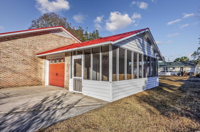 view of home's exterior with metal roof, an attached garage, driveway, and a sunroom