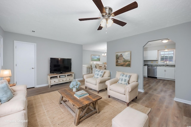 living room featuring arched walkways, ceiling fan with notable chandelier, baseboards, and wood finished floors