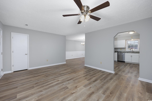 unfurnished living room featuring ceiling fan with notable chandelier, a textured ceiling, wood finished floors, arched walkways, and baseboards