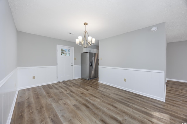 unfurnished room with wood finished floors, visible vents, a wainscoted wall, a textured ceiling, and a chandelier