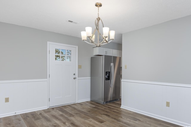 unfurnished dining area featuring visible vents, a wainscoted wall, a textured ceiling, dark wood finished floors, and an inviting chandelier