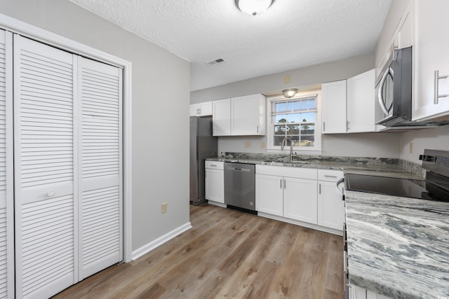 kitchen featuring visible vents, light wood-style flooring, a sink, stainless steel appliances, and white cabinets