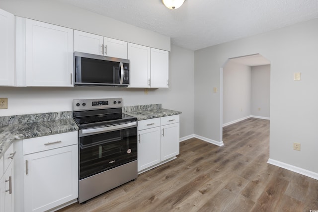 kitchen with arched walkways, white cabinetry, stainless steel appliances, and light wood-style floors