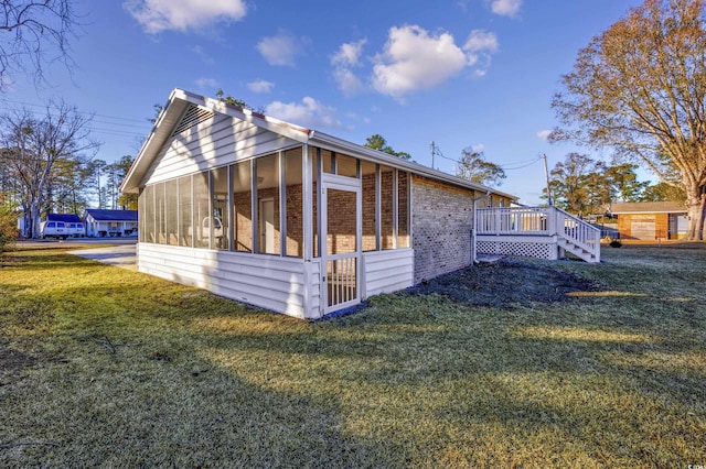 view of property exterior with a lawn, brick siding, a sunroom, and a wooden deck