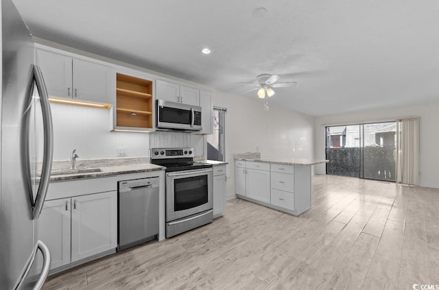 kitchen with light stone countertops, appliances with stainless steel finishes, light wood-style floors, white cabinetry, and a sink