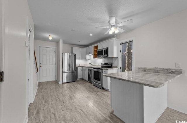 kitchen featuring open shelves, white cabinetry, appliances with stainless steel finishes, a peninsula, and light wood finished floors