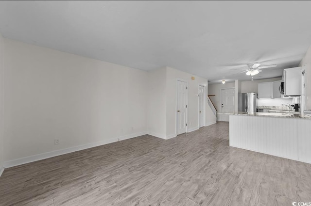 unfurnished living room featuring a sink, baseboards, light wood-style floors, and ceiling fan