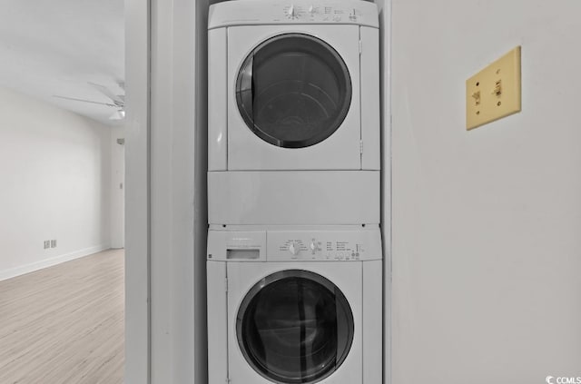 laundry area featuring wood finished floors, a ceiling fan, baseboards, stacked washing maching and dryer, and laundry area