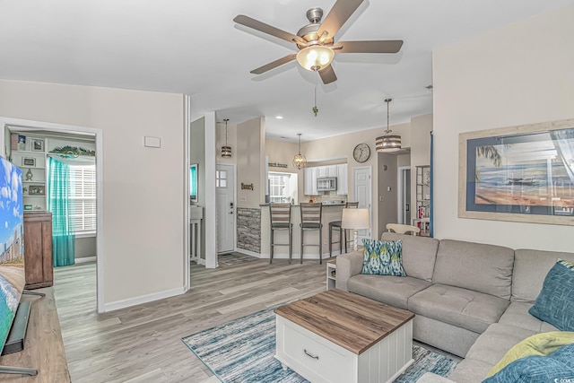 living room featuring light wood-style floors, baseboards, and a ceiling fan