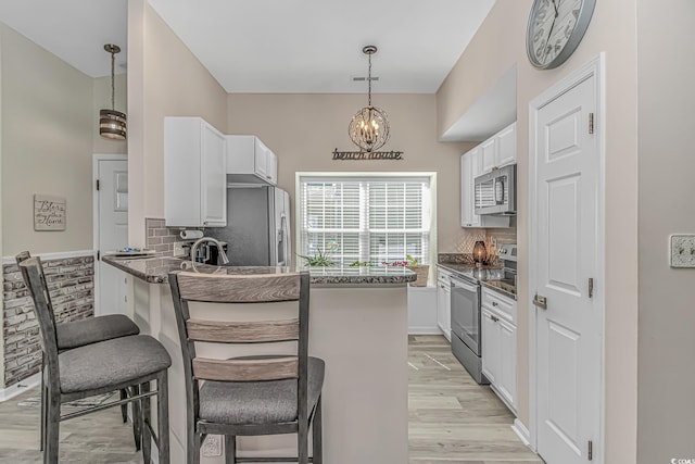 kitchen with stainless steel appliances, white cabinets, light wood-type flooring, a peninsula, and a kitchen breakfast bar