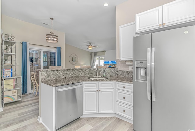 kitchen featuring light wood finished floors, appliances with stainless steel finishes, white cabinets, a sink, and a peninsula