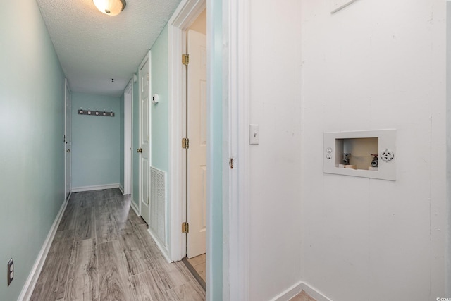 hall with light wood finished floors, visible vents, a textured ceiling, and baseboards