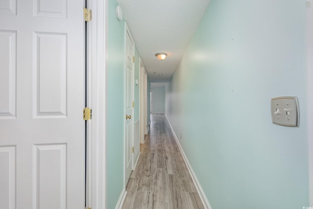 hall featuring light wood finished floors, a textured ceiling, and baseboards