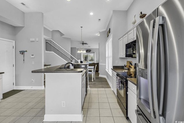 kitchen featuring light tile patterned floors, dark countertops, black appliances, and a kitchen island with sink