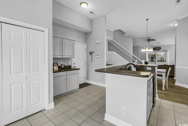 kitchen featuring light tile patterned floors, dark countertops, an inviting chandelier, and a kitchen island with sink