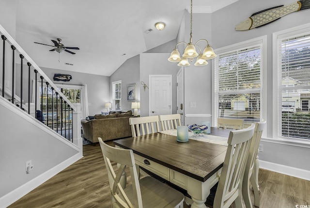 dining room with ceiling fan with notable chandelier, wood finished floors, baseboards, stairs, and vaulted ceiling