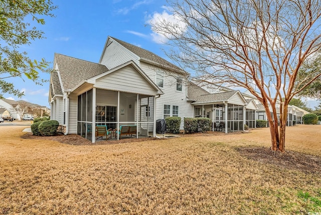 back of property featuring a lawn, a shingled roof, and a sunroom