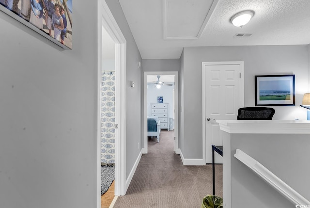 corridor featuring visible vents, baseboards, a textured ceiling, carpet flooring, and an upstairs landing