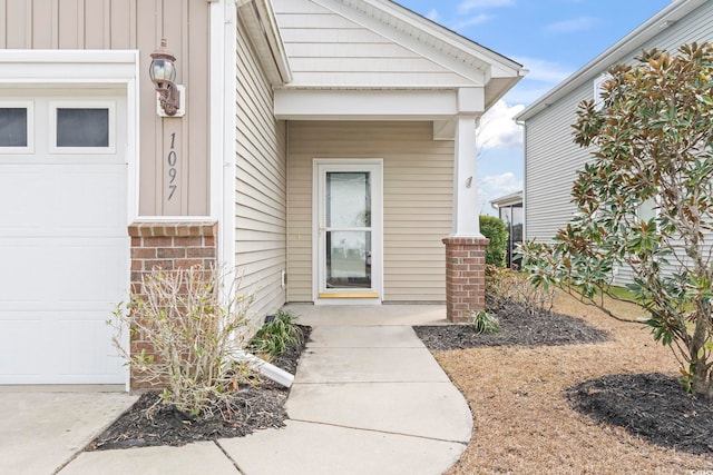 doorway to property featuring board and batten siding, an attached garage, and brick siding