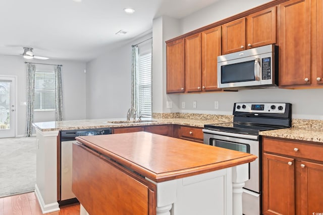 kitchen with brown cabinets, a sink, a center island, appliances with stainless steel finishes, and a peninsula