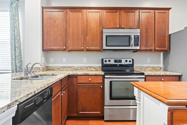 kitchen with a sink, light stone countertops, light wood-style floors, and stainless steel appliances
