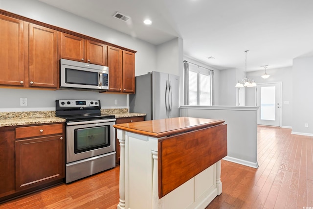 kitchen featuring light wood-type flooring, brown cabinets, a notable chandelier, a center island, and stainless steel appliances