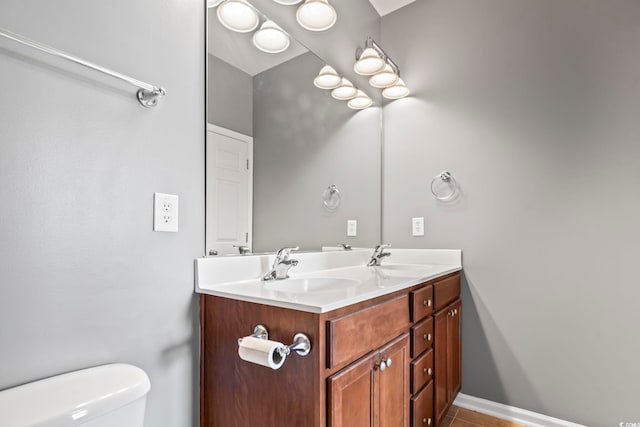 bathroom featuring a sink, baseboards, toilet, and double vanity