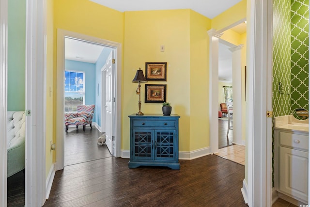 corridor featuring baseboards, dark wood-type flooring, and ornate columns