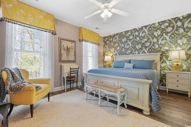 bedroom with visible vents, wallpapered walls, ceiling fan, baseboards, and wood finished floors