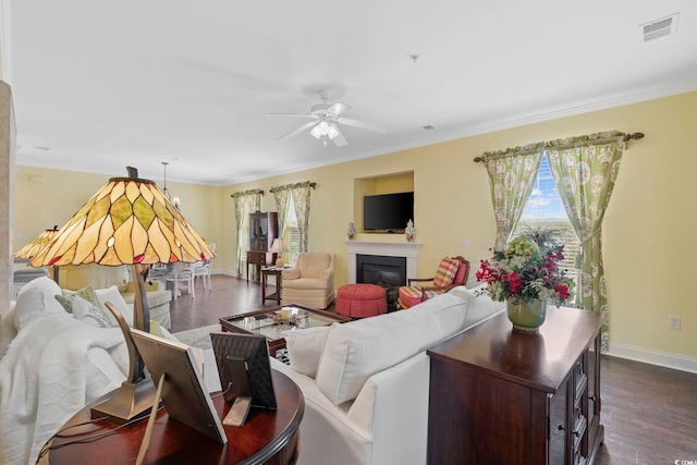 living area with baseboards, visible vents, dark wood finished floors, a glass covered fireplace, and crown molding