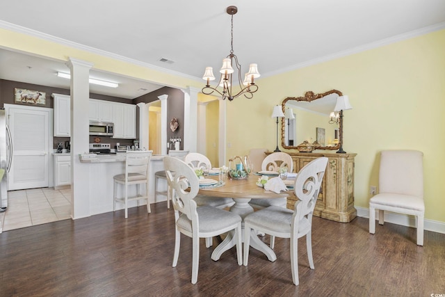 dining area featuring visible vents, crown molding, light wood-style flooring, a notable chandelier, and ornate columns