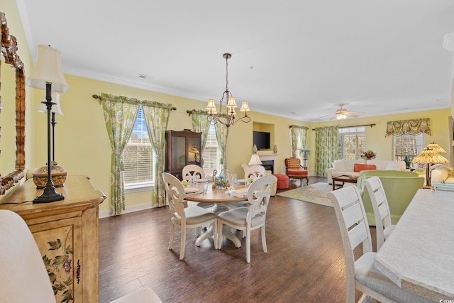 dining space with dark wood-style floors, baseboards, visible vents, a fireplace, and ornamental molding