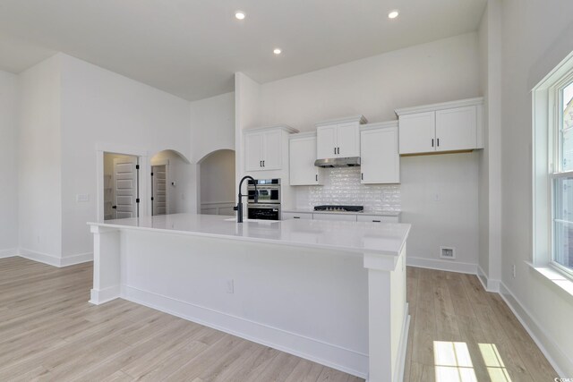 4028 Bucolic Loop, Myrtle Beach, SC 29588 - kitchen featuring stovetop, backsplash, an island with sink, arched walkways, and white cabinets