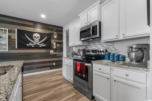 kitchen with stainless steel appliances, decorative backsplash, white cabinets, light wood-style floors, and wood walls