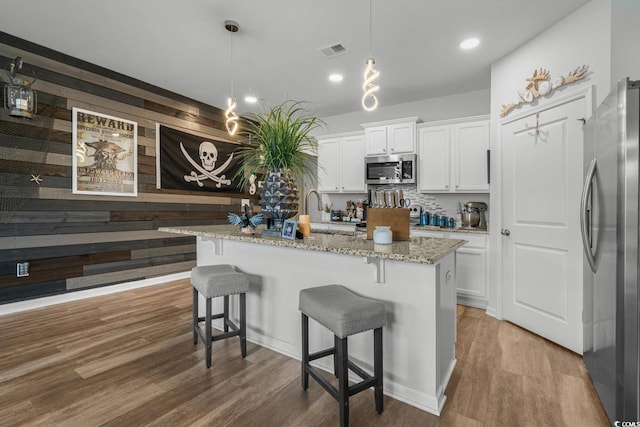 kitchen with light stone counters, wood finished floors, visible vents, appliances with stainless steel finishes, and white cabinetry