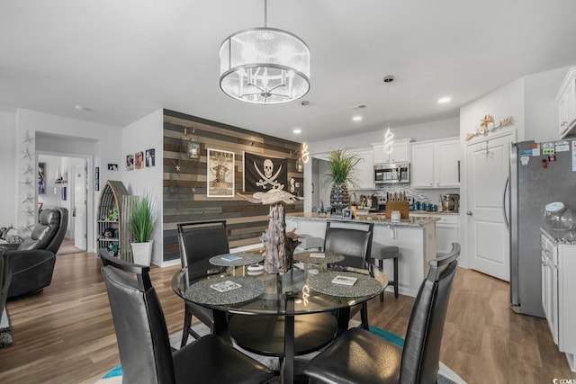 dining area featuring an accent wall, recessed lighting, wood finished floors, and a chandelier