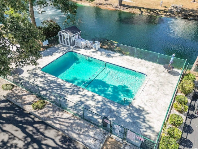 pool with an outdoor structure, fence, a water view, and a patio