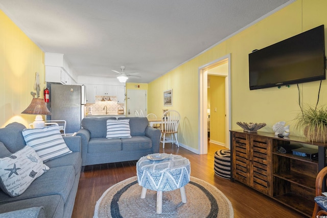 living area featuring ornamental molding, ceiling fan, baseboards, and dark wood-style flooring