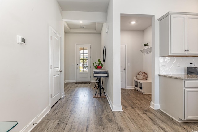 hallway with baseboards, light wood-style floors, a tray ceiling, and visible vents