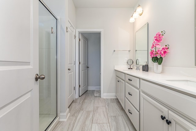 full bath featuring double vanity, baseboards, a stall shower, and a sink