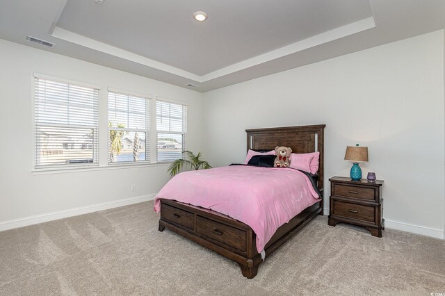 bedroom with a tray ceiling, light colored carpet, baseboards, and visible vents