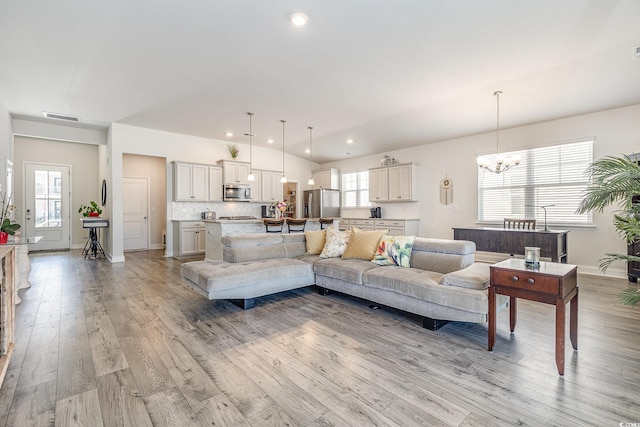 living room featuring light wood finished floors, plenty of natural light, a notable chandelier, and visible vents