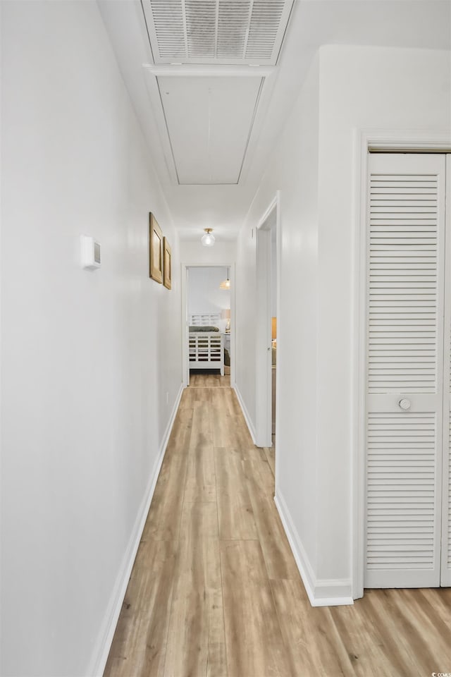 hall featuring attic access, baseboards, visible vents, and light wood-type flooring