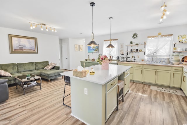 kitchen with light wood finished floors, open floor plan, light countertops, a kitchen breakfast bar, and a sink