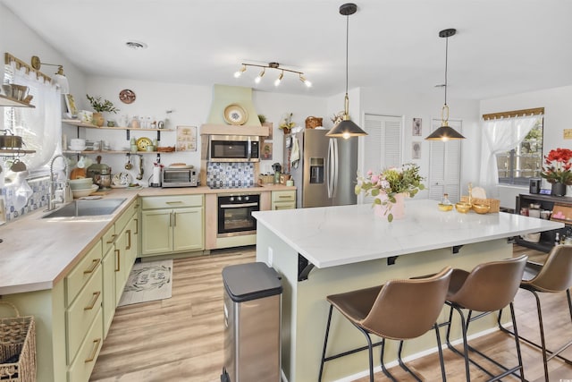 kitchen featuring open shelves, a sink, light wood-style floors, appliances with stainless steel finishes, and green cabinets