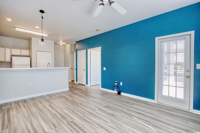 unfurnished living room with a sink, baseboards, light wood-style floors, and a ceiling fan