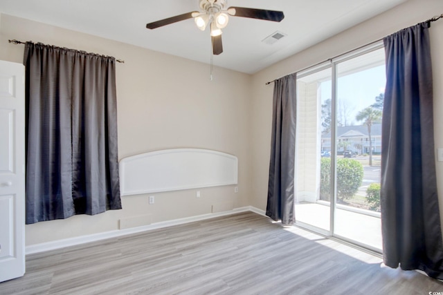 unfurnished room with ceiling fan, wood finished floors, visible vents, and baseboards