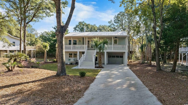 coastal home featuring a porch, stairs, concrete driveway, a front lawn, and metal roof