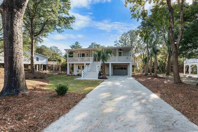 raised beach house with stairway, a garage, concrete driveway, and a front lawn